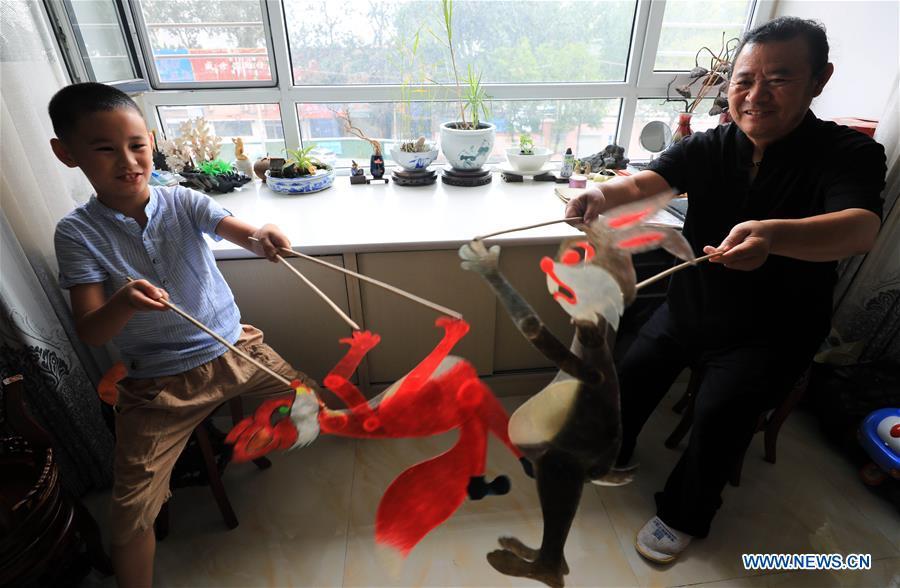 Li Wei and his grandson perform a shadow puppet show in Jinan, east China\'s Shandong Province, July 11, 2018. Li, 63, is the son of Jinan shadow puppet show master Li Xingtang. He learned shadow puppet performance from his father in childhood. After his father passed away 11 years ago, Li Wei took over the task of developing and innovating the art of Jinan puppet show. Since last summer, Li has kept on presenting traditional shadow puppet plays at the Baihuazhou scenic area in Jinan every weekend for free. (Xinhua/Zhao Xiaoming)