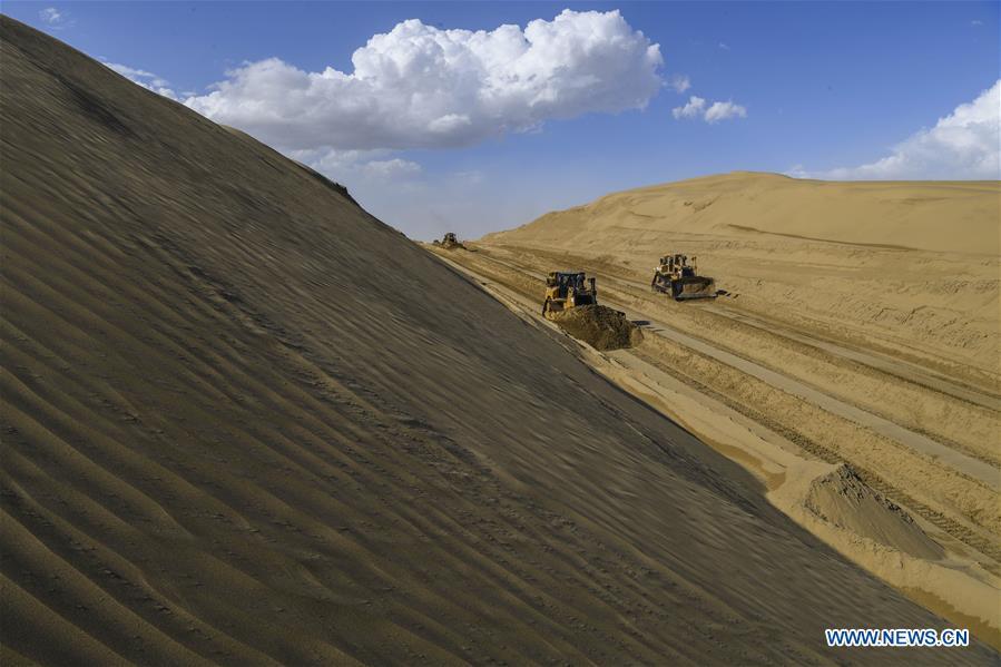 Vehicles work at a desert road construction site in Taklimakan desert in northwest China\'s Xinjiang Uygur Autonomous Region, July 5, 2018. An over 300-km-long desert road, linking Xinjiang\'s Yuli County to remote Qiemo County, is now under construction. It\'s the third that-kind-of road crossing China\'s largest desert Taklimakan nicknamed \
