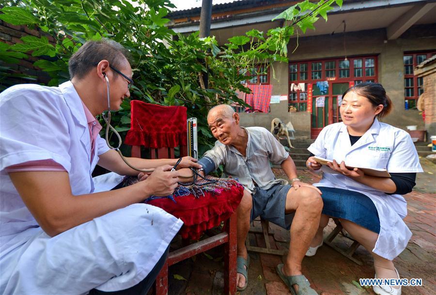 Doctors Zhai Dalong (L) and Wang Cuihong (R) measure blood pressure for a patient in Xudi Village of Daming County in Handan, north China\'s Hebei Province, Aug. 16, 2018. Zhai and Wang are husband and wife. A large number of medical practitioners are active in China\'s rural areas where health care is still underdeveloped. Under adverse working conditions, they have carried forward the humanitarian spirit and devoted themselves to the health of rural citizens. China will mark its first Medical Worker\'s Day on Aug. 19, 2018. (Xinhua/Wang Xiao)