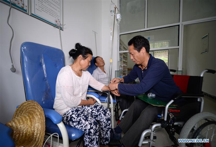 Doctor Sun Qingyong (R) gives a patient intravenous injection at a clinic in Shaluo Village of Guanghuojie Township in Ningshan County, Ankang, northwest China\'s Shaanxi Province, Aug. 15, 2018. Sun became paraplegic in a traffic accident 22 years ago. He soon started offering medical treatment to his fellow villagers on a wheelchair. A large number of medical practitioners are active in China\'s rural areas where health care is still underdeveloped. Under adverse working conditions, they have carried forward the humanitarian spirit and devoted themselves to the health of rural citizens. China will mark its first Medical Workers\' Day on Aug. 19, 2018. (Xinhua/Liu Xiao)
