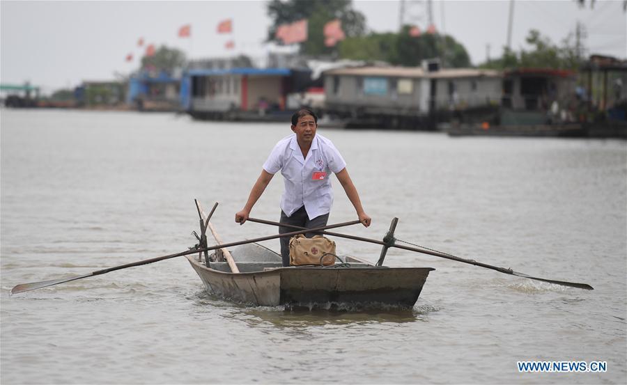 Doctor Li Shaoyou rows a boat on his way to a patient\'s home in Mudundao Village of Bancheng Township, Sihong County, east China\'s Jiangsu Province, June 27, 2018. Li has been offering medical services to fishermen around the Hongze Lake for more than three decades. A large number of medical practitioners are active in China\'s rural areas where health care is still underdeveloped. Under adverse working conditions, they have carried forward the humanitarian spirit and devoted themselves to the health of rural citizens. China will mark its first Medical Workers\' Day on Aug. 19, 2018. (Xinhua/Ji Chunpeng)