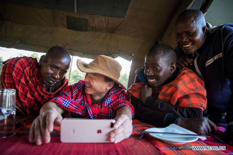 Chinese wildlife conservationist Zhuo Qiang (2nd L) watches a football match with locals at Ol Kinyei conservancy in Maasai Mara, Kenya, July 7, 2018. The founder and Chairman of Mara Conservation Fund (MCF) Zhuo Qiang, a 45-year-old Chinese, has pioneered outstanding wildlife conservation projects in the world famous Maasai Mara ecosystem. Ol Kinyei is among the conservancies benefiting from his activities. Around it, he has built three lion proof boas preventing the wildlife conflict with the adjacent communities. He was officially adopted as a son of the Maasai\'s Ol Kinyei conservation group in 2015, owing to his unwavering friendship with the pastoralists. Zhuo\'s anti-poaching drives in the East African nation expresses the increasing collaboration between Kenyan and China in ending the killing of rhinos, elephants and lions. (Xinhua/Lyu Shuai)