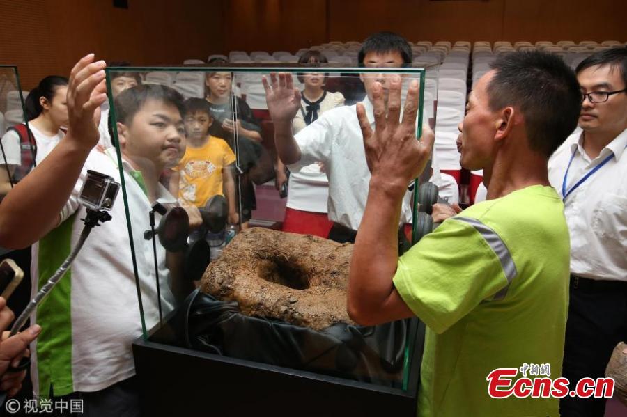 Visitors view a meteorite crater exhibited at a press conference held by Shanghai Planetarium in east China\'s Shanghai, Aug. 25, 2018. Shanghai Planetarium on Saturday announced plans to house meteorites recovered from a meteor fireball that happened over the sky in Jinghong City of southwest China\'s Yunnan Province in June. The planetarium, which is under construction, will be a branch of the Shanghai Science & Technology Museum. The museum staff have successfully recovered more than 500 pieces of meteorites, about 50 kg in total, said Lin Qing, deputy director in charge of the planetarium construction, at a press conference Saturday. (Photo/VCG)