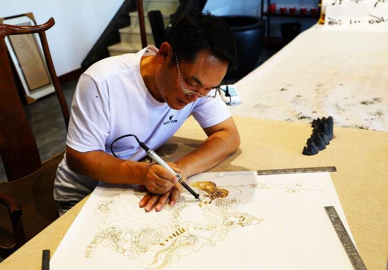 Zhang Ge guides a woodburning pen to create a pyrography artwork.  (Photo provided to chinadaily.com.cn)

Zhang Ge, an artist in Datong, North China\'s Shanxi Province, has created a series of pyrography, artworks themed on famous landscapes, historical figures and stories about the city, such as the Yungang Grottoes and Xuankong Temple.

Pyrography, or woodburning, is the art of decorating wood or other materials resulting from the controlled application of a heated object, such as a woodburning pen.

\
