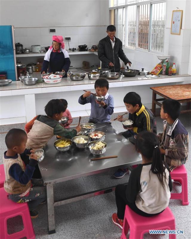 Wang Zhengxiang (R, back) and his wife prepare meals for the students at Ayiyang Primary School in Sanmeng Village of Luquan Yi and Miao Autonomous County, southwest China\'s Yunnan Province, Sept. 6, 2018. One teacher, eight students, none was and will be given up thanks to rural teacher Wang Zhengxiang. Wang Zhengxiang of Miao ethnic group, 56, is the only teacher and has been teaching at the remote village primary school of Ayiyang for 38 years. Ayiyang Primary School, lying at an altitude of 2,600 meters above sea level and surrounded by mountains, is not within easy reach of outside world. There are just eight students at the school. Yet Wang takes care of his students with love, consideration and strong sense of responsibility. He buys shoes and daily goods for poverty-stricken students with his own money, and he has tried every means to keep those who wanted to drop out due to economic insufficiency. \