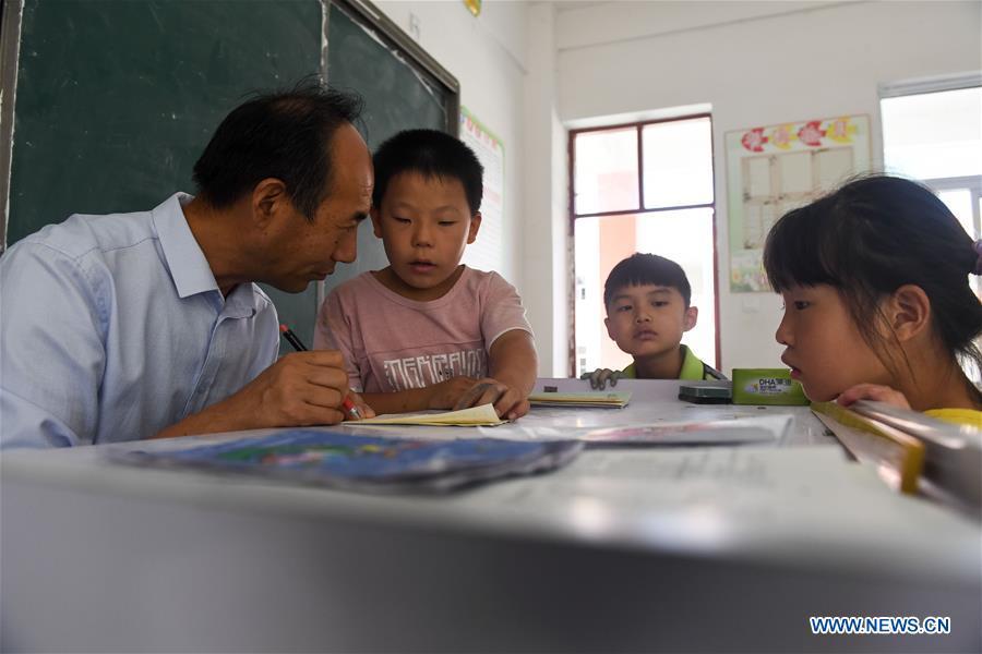 With help of students, Guo Yue corrects students\' papers in Guozhai Primary School, Taihe County of east China\'s Anhui Province, Sept. 7, 2018. Guo, suffering a chronic loss of eyesight due to an illness a few years after he began his career as teacher in 1986, managed to keep teaching in the school. Almost totally blind, Guo also teaches in music and ethical education classes in addition to Chinese. (Xinhua/Zhang Duan)