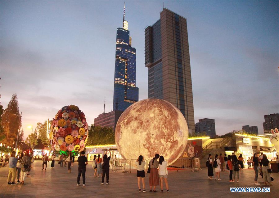 Pedestrians look at a moon installation set up to mark the upcoming Mid-Autumn Festival at a plaza in Nanjing, east China\'s Jiangsu Province, Sept. 23, 2018. (Xinhua/Liu Jianhua)