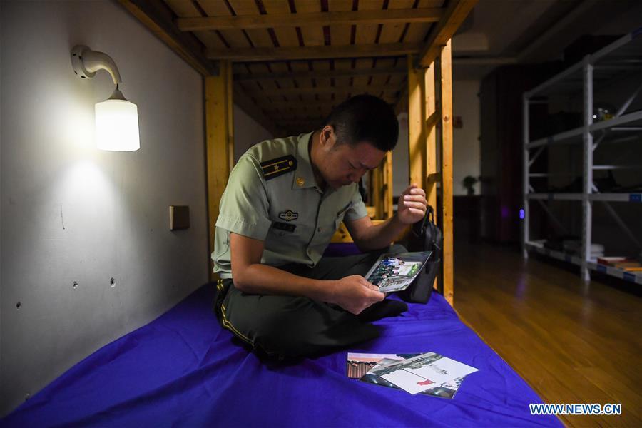 Wang Zhiguo looks at family photos in the dormitory in Nanjing, capital of east China\'s Jiangsu Province, Aug. 7, 2018. Wang Jicai, who used to be head of the militia post on Kaishan Island in Jiangsu Province, started working on the island in the Yellow Sea with his wife in 1986. He died of sudden illness while on duty in July of 2018 at the age of 58. Wang Zhiguo, son of Wang Jicai, became a frontier defence policeman after his graduation from Nanjing University of Aeronautics and Astronautics in 2013. He had been assigned to many security tasks for major events during 5 years\' working. (Xinhua/Li Xiang)