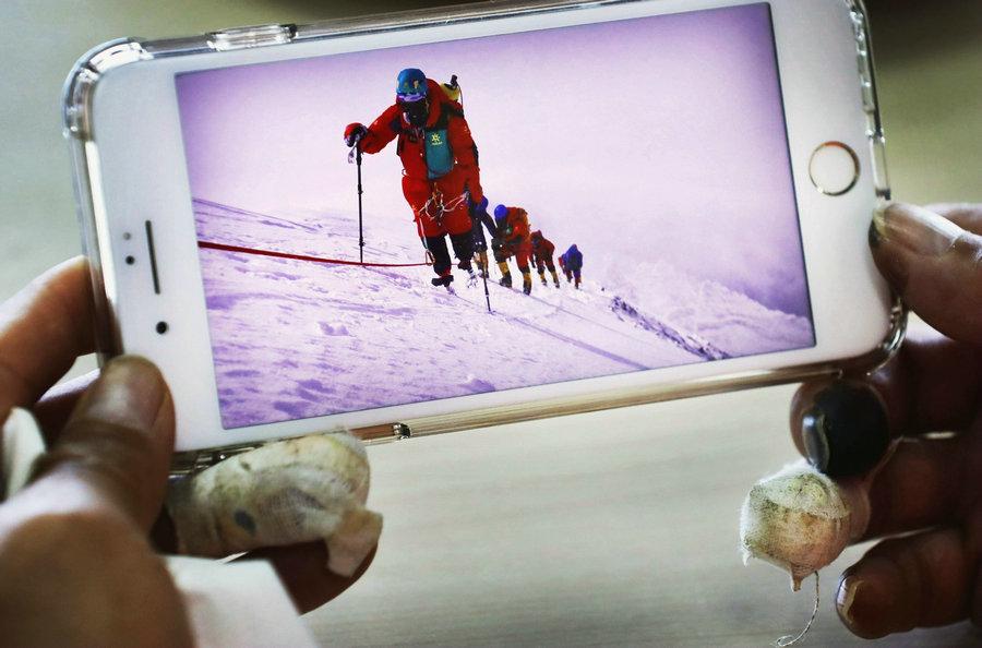 Xia looks at the photos and recalls the experience of climbing Qomolangma.(Photo/China Daily)

\