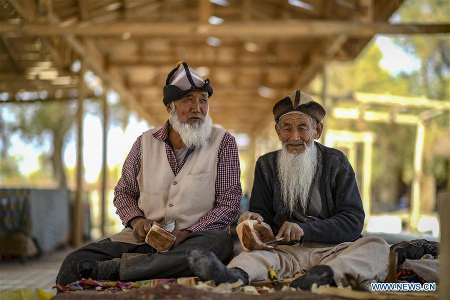 Two residents make models of a special kind of dugout canoe made of desert poplar in Lop Nur People Village of Yuli County, northwest China\'s Xinjiang Uygur Autonomous Region, Oct. 16, 2018. The Lop Nur people depended basically on fishing for livelihood and developed a distinct culture based on their special lifestyle. Located in Tarim basin, Yuli is known for its natural scenery and ethnic culture and keeps attracting numerous tourists from at home and abroad. From Oct. 1 to 16, 2018, Yuli County has received more than 230,000 visitors, with a year-on-year increase of 31.46 percent. (Xinhua/Zhao Ge)
