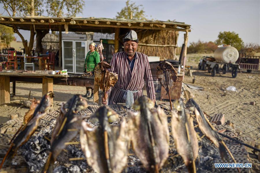 A resident makes roast fish at the Lop Nur People Village of Yuli County, northwest China\'s Xinjiang Uygur Autonomous Region, Oct. 16, 2018. The Lop Nur people depended basically on fishing for livelihood and developed a distinct culture based on their special lifestyle. Located in Tarim basin, Yuli is known for its natural scenery and ethnic culture and keeps attracting numerous tourists from at home and abroad. From Oct. 1 to 16, 2018, Yuli County has received more than 230,000 visitors, with a year-on-year increase of 31.46 percent. (Xinhua/Zhao Ge)