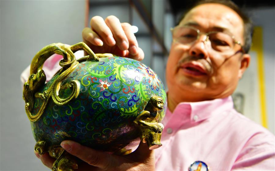 Lin Hui presents an enamelwork in Putian, southeast China\'s Fujian Province, Oct. 18, 2018. Lin Hui is an intangible cultural heritage inheritor of Lin\'s cloisonne, or copper padding thread weaving enamel, a kind of traditional Chinese handicrafts. (Xinhua/Wei Peiquan)