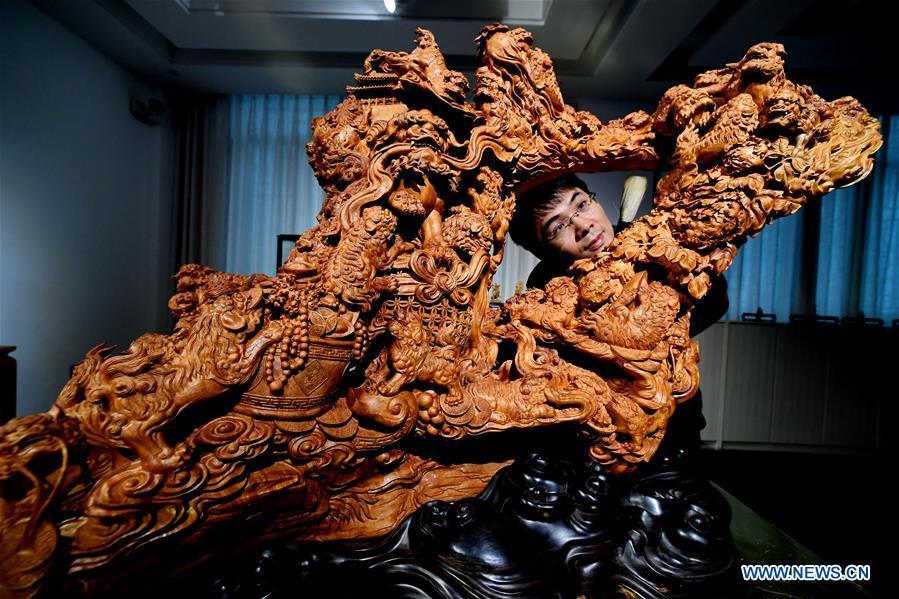 Lin Jianjun cleans his wood carving at a studio in Putian, southeast China\'s Fujian Province, Oct. 23, 2018. Lin Jianjun, who learnt wood carving at the age of 16, has studied the making skill of this traditional artwork for more than 20 years. In 2014, Lin got married with Chen Qin. The wife was influenced by her husband and got interested in wood carving. She developed the wood carving by combining a traditional skill to make wood carving inlaid with gold and silver. The couple meanwhile try to promote the Putian wood carving by giving lessons, instructing apprentices and displaying their works to the public. In 2018, Lin was appointed as the inheritor of the wood carving skill, a provincial-level intangible cultural heritage. (Xinhua/Zhang Guojun)