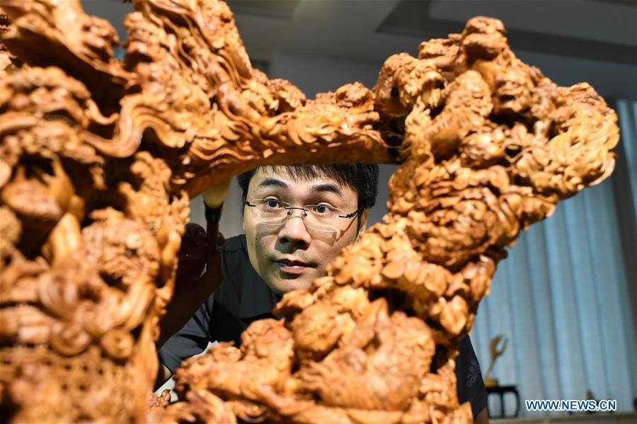 Lin Jianjun cleans his wood carving at a studio in Putian, southeast China\'s Fujian Province, Oct. 23, 2018. Lin Jianjun, who learnt wood carving at the age of 16, has studied the making skill of this traditional artwork for more than 20 years. In 2014, Lin got married with Chen Qin. The wife was influenced by her husband and got interested in wood carving. She developed the wood carving by combining a traditional skill to make wood carving inlaid with gold and silver. The couple meanwhile try to promote the Putian wood carving by giving lessons, instructing apprentices and displaying their works to the public. In 2018, Lin was appointed as the inheritor of the wood carving skill, a provincial-level intangible cultural heritage. (Xinhua/Jiang Kehong)