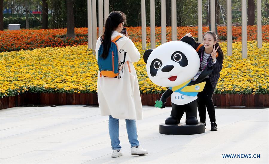 A volunteer for the upcoming China International Import Expo (CIIE) poses for a photo with the mascot \