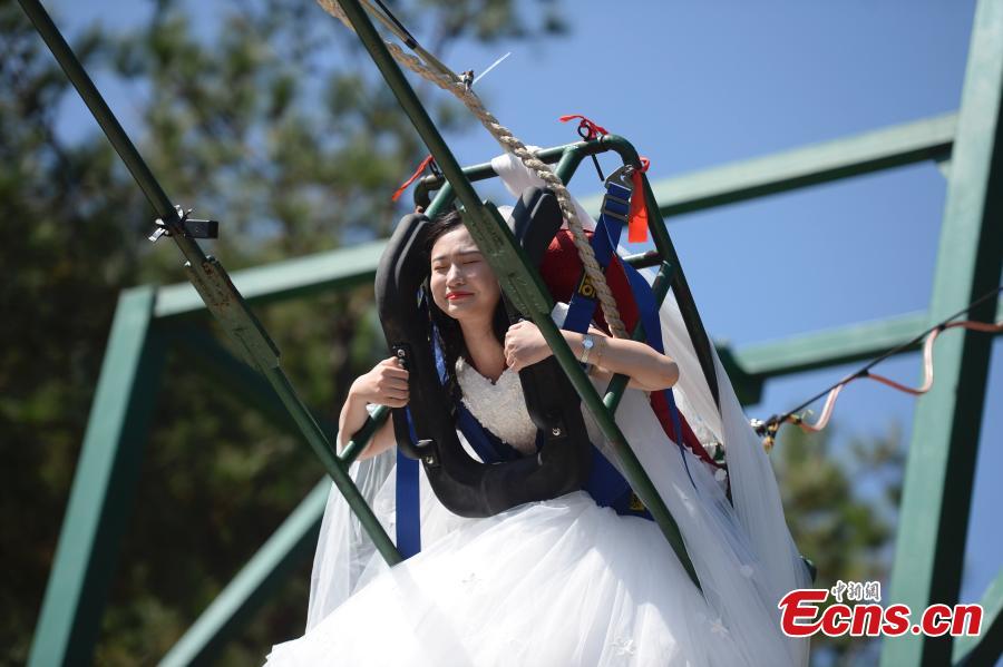 A woman dons a wedding dress to pose for a photo while sitting on a swing that is built close to a cliff at the Shiniuzhai National Geological Park in Pingjiang County, Central China\'s Hunan Province, Oct. 28, 2018. (Photo: China News Service/Yang Huafeng)