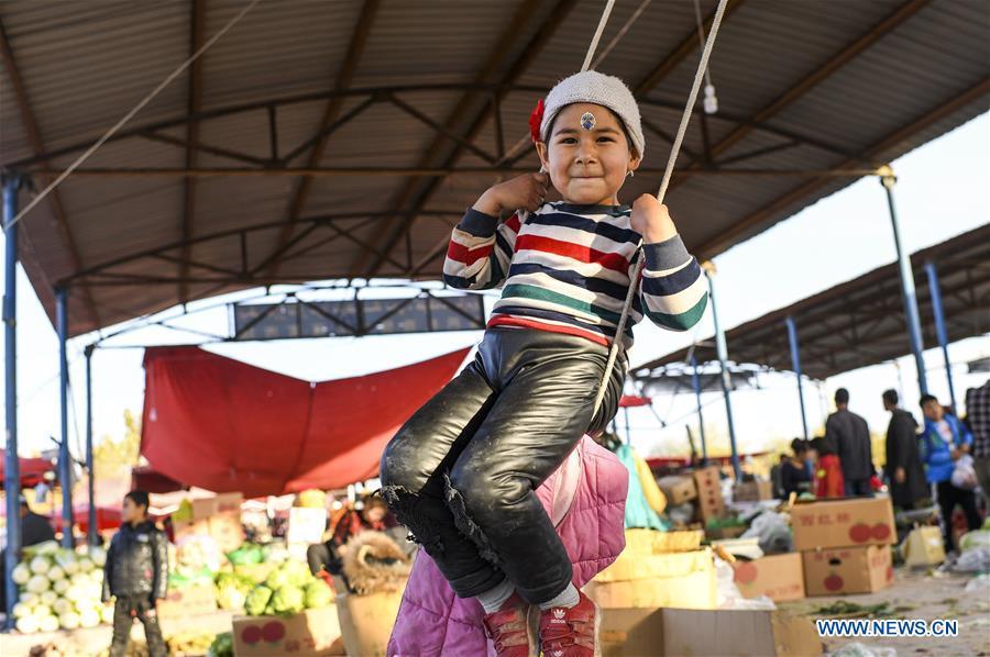 A girl plays a swing at a Sunday bazaar in Bachu County, northwest China\'s Xinjiang Uygur Autonomous Region, Oct. 28, 2018. (Xinhua/Hu Huhu)
