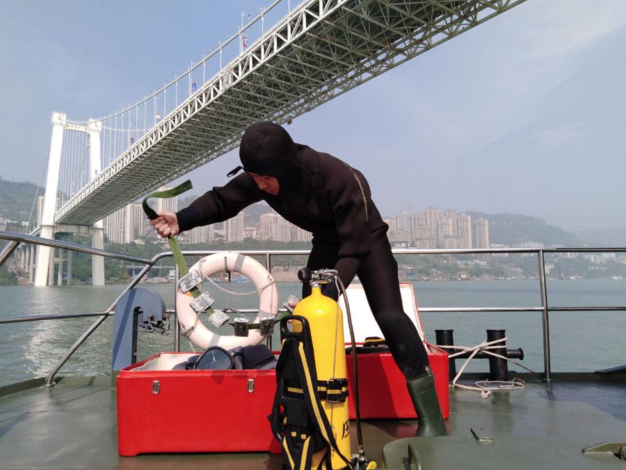 A diver from the armed police force stationed in Chongqing prepares to search the water on Sunday. (Photo by ZHOU YUKAI/FOR CHINA DAILY)
The driver of the car, identified as Kuang, was taken to the hospital with soft tissue injuries. The bus driver, surnamed Ran, is among the missing, the police said.
The cause of the accident is under investigation.
A rescue worker at the site said that the bridge stands more than 50 meters above the water and that the bus had sunk 68 meters below the surface.
Firefighters, public security officials and police officers were working on a plan to recover the bus.
The Ministry of Emergency Management dispatched 11 professional divers, a medical worker capable of deep diving and a salvage boat to assist in the rescue operation.
vThe four-lane Second Yangtze River Bridge opened to traffic in June 2003. It carries a daily average of more than 60,000 vehicles and over 200,000 commuters, according to the Wanzhou government.