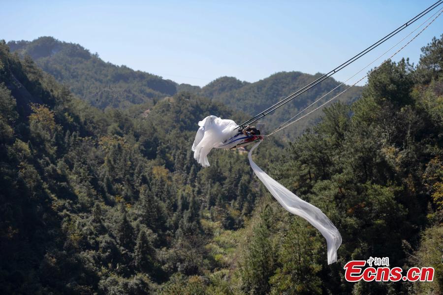 A woman dons a wedding dress to pose for a photo while sitting on a swing that is built close to a cliff at the Shiniuzhai National Geological Park in Pingjiang County, Central China\'s Hunan Province, Oct. 28, 2018. (Photo: China News Service/Yang Huafeng)