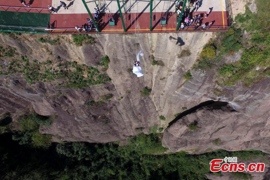 A woman dons a wedding dress to pose for a photo while sitting on a swing that is built close to a cliff at the Shiniuzhai National Geological Park in Pingjiang County, Central China\'s Hunan Province, Oct. 28, 2018. (Photo: China News Service/Yang Huafeng)
