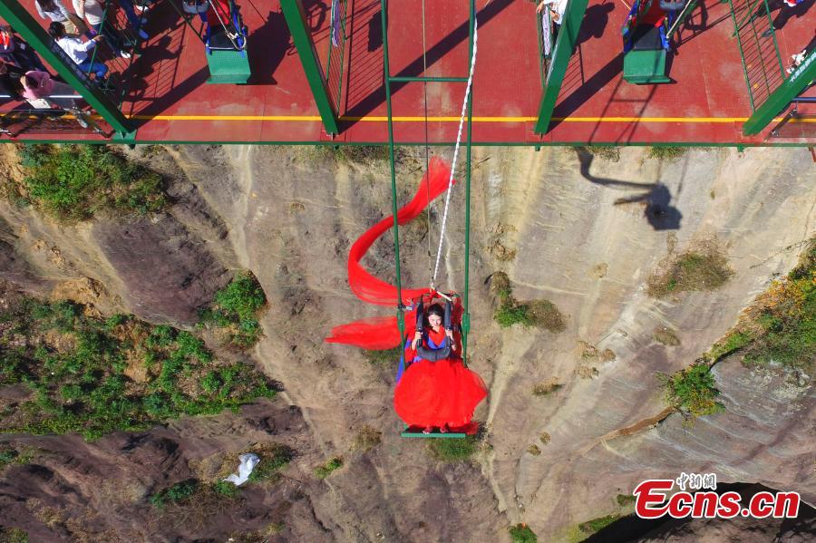 A woman dons a wedding dress to pose for a photo while sitting on a swing that is built close to a cliff at the Shiniuzhai National Geological Park in Pingjiang County, Central China\'s Hunan Province, Oct. 28, 2018. (Photo: China News Service/Yang Huafeng)