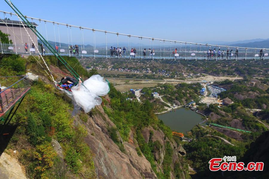 A woman dons a wedding dress to pose for a photo while sitting on a swing that is built close to a cliff at the Shiniuzhai National Geological Park in Pingjiang County, Central China\'s Hunan Province, Oct. 28, 2018. (Photo: China News Service/Yang Huafeng)