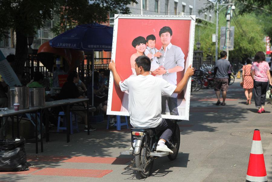 A man carries a photo of a happy family on the back of an electric bicycle in Neiwubu Street, Dongcheng district, Beijing, on June 8, 2012. (Photo by ZHANG JUSHENG/FOR CHINA DAILY)