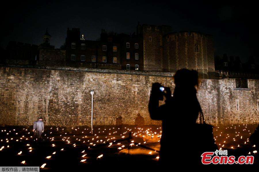 A woman photographs lit torches that are part of the installation \