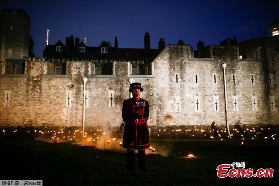 A Yeoman of the Guard stands amongst lit torches that are part of the installation \