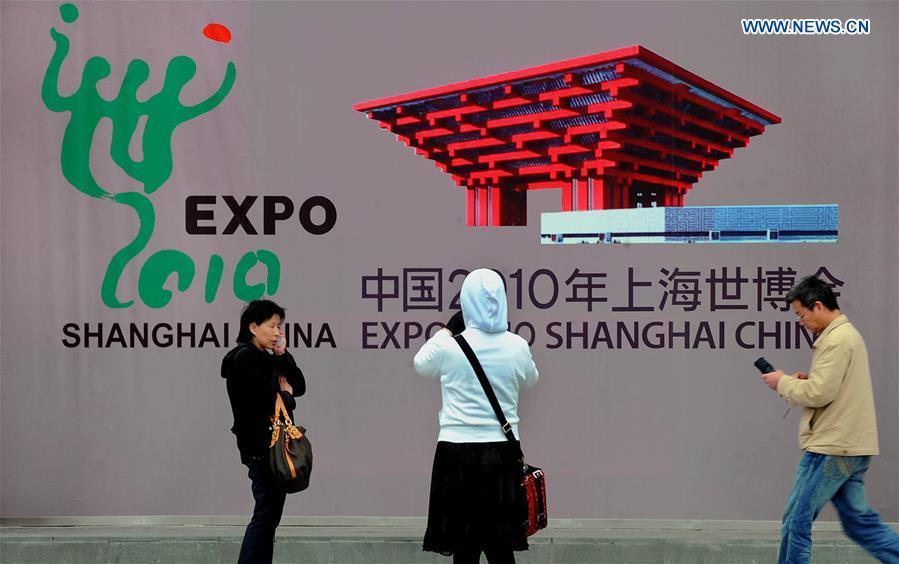 People are seen in front of a billboard of the Shanghai 2010 World Expo in Shanghai, east China, April 22, 2010. (Xinhua/Wang Song)