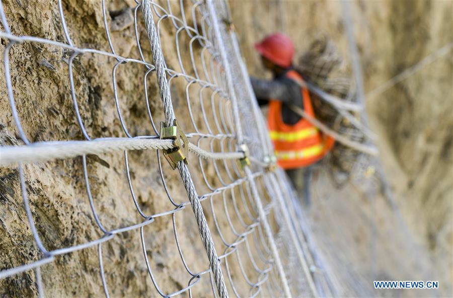A construction worker carries equipment on a cliff at a road section in the Tajik Autonomous County of Taxkorgan, northwest China\'s Xinjiang Uygur Autonomous Region, Nov. 12, 2018. The job of this team of construction workers is to install protective facilities on the cliff of risky road sections in the mountainous areas in Xinjiang, protecting pedestrians and vehicles from fallen stones. (Xinhua/Hu Huhu)