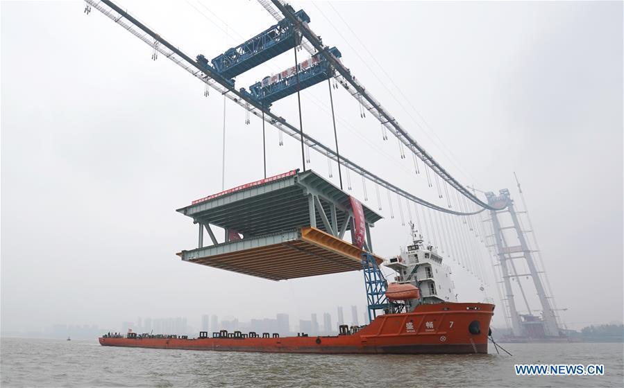 A 1,000-tonne steel beam is lifted to be installed at the construction site of the Yangsigang Bridge across the Yangtze River in Wuhan, capital of central China\'s Hubei Province, on Nov. 15, 2018. Construction of a double-deck suspension bridge with the longest span in the world is expected to be completed in October 2019, said an engineer working on the project. The bridge, with a 1,700-meter-long main span across the Yangtze River in Wuhan, saw the first steal beam installed for the bridge deck Thursday. (Xinhua/Cheng Min)