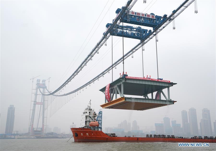 A 1,000-tonne steel beam is lifted to be installed at the construction site of the Yangsigang Bridge across the Yangtze River in Wuhan, capital of central China\'s Hubei Province, on Nov. 15, 2018. Construction of a double-deck suspension bridge with the longest span in the world is expected to be completed in October 2019, said an engineer working on the project. The bridge, with a 1,700-meter-long main span across the Yangtze River in Wuhan, saw the first steal beam installed for the bridge deck Thursday. (Xinhua/Cheng Min)
