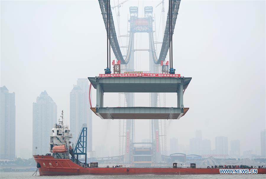 A 1,000-tonne steel beam is lifted to be installed at the construction site of the Yangsigang Bridge across the Yangtze River in Wuhan, capital of central China\'s Hubei Province, on Nov. 15, 2018. Construction of a double-deck suspension bridge with the longest span in the world is expected to be completed in October 2019, said an engineer working on the project. The bridge, with a 1,700-meter-long main span across the Yangtze River in Wuhan, saw the first steal beam installed for the bridge deck Thursday. (Xinhua/Cheng Min)