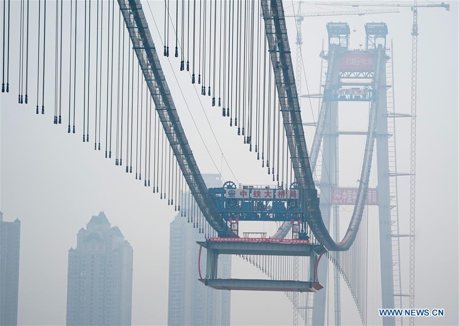 The installation of a 1,000-tonne steel beam is finished at the construction site of the Yangsigang Bridge across the Yangtze River in Wuhan, capital of central China\'s Hubei Province, on Nov. 15, 2018. Construction of a double-deck suspension bridge with the longest span in the world is expected to be completed in October 2019, said an engineer working on the project. The bridge, with a 1,700-meter-long main span across the Yangtze River in Wuhan, saw the first steal beam installed for the bridge deck Thursday. (Xinhua/Cheng Min)