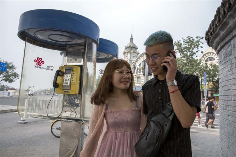 A couple walks past a deserted telephone box while the man talks on a mobile phone in Qianmen, Beijing in 2018. (Photo provided to chinadaily.com.cn)