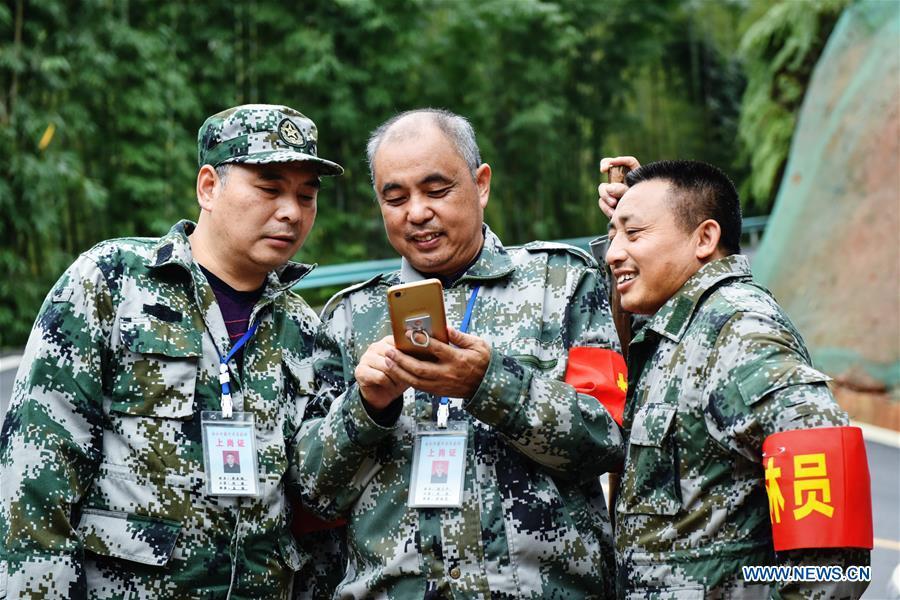 Forest ranger Tang Xiaoping (C) shows his photos of family members with colleagues at Hushi forestry farm in Chishui City, southwest China\'s Guizhou Province, Oct. 24, 2018. Chishui is famous for its bamboo forest. To guard the bamboo, forest rangers need to patrol for all year round. At the Hushi forestry farm, there is a patrol group consisting of a dozen of forest rangers. They are in charge of about an area of 2,400 hectares. Loneliness is one of the difficulties they need to face as they can only go back home after one-week work. But all of them stay to keep working after those years as they love the bamboo forest and are determined to guard it. (Xinhua/Li Mangmang)