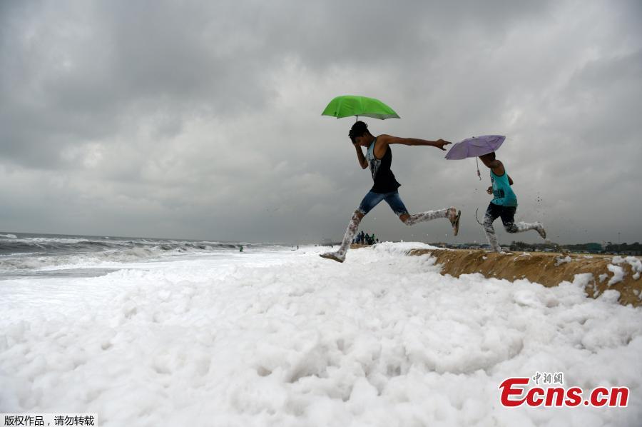 Umbrella-toting Indian youths jump over foamy discharge, caused by pollutants, as it mixes with the surf at a beach in Chennai on November 22, 2018. - High levels of sewage and industrial waste was claimed to be the cause of the foam, officials said. (Photo/Agencies)