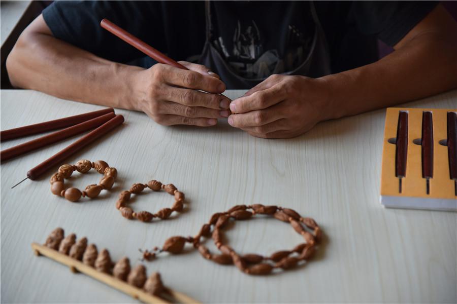 Zhu Haiyang does olive pit carving at his home in September of last year. (Photo by Qian Lei for chinadaily.com.cn)