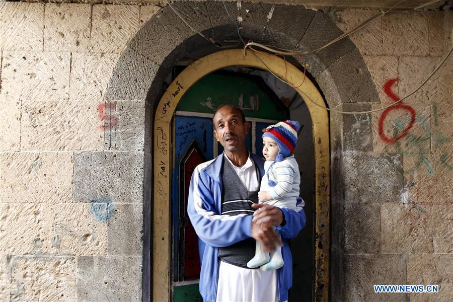Ahmed al-Sharafi holding his seven-month-old child Omar stands at the door of his house in Sanaa, Yemen, on Dec. 9, 2018. An estimated 85,000 children under the age of five may have died from extreme hunger between April 2015 and October 2018, according to the latest data released by Save the Children, an international organization for children\'s rights. (Xinhua/Mohammed Mohammed)