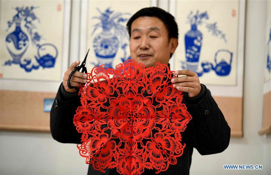 Niu Shimin displays his work of paper cutting at his workshop in Wuji County, north China\'s Hebei Province, Dec. 19, 2018. Niu Shimin has been interested in paper cutting since he was young. He created his own style through over 30 years of practicing and was awarded as the inheritor of this provincial intangible cultural heritage in 2008. (Xinhua/Chen Qibao)
