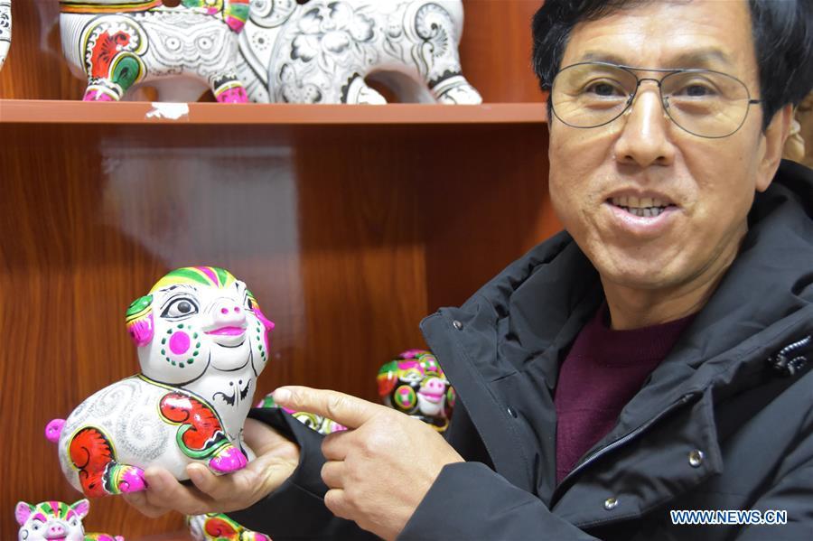 Clay sculpture master Hu Xinming shows a clay pig sculpture he designed in Liuying Village of Fengxiang County, northwest China\'s Shaanxi Province, Dec. 20, 2018. Artists of Liuying Village of Fengxiang County, known as the hometown of clay sculpture, were busy making clay sculptures to greet the upcoming Chinese lunar new year, the Year of the Pig. (Xinhua/Du Honggang)