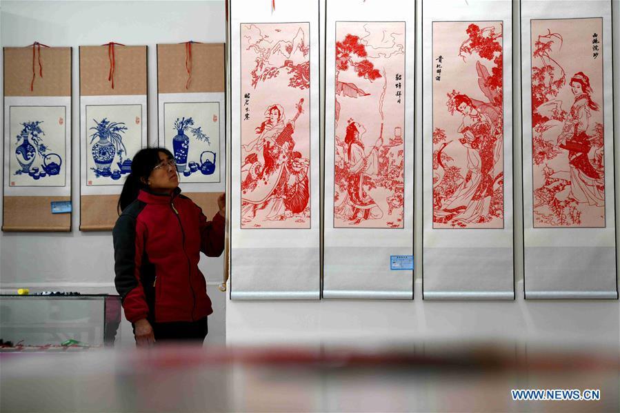A visitor looks at Niu Shimin\'s works of paper cutting at the workshop in Wuji County, north China\'s Hebei Province, Dec. 19, 2018. Niu Shimin has been interested in paper cutting since he was young. He created his own style through over 30 years of practicing and was awarded as the inheritor of this provincial intangible cultural heritage in 2008. (Xinhua/Chen Qibao)