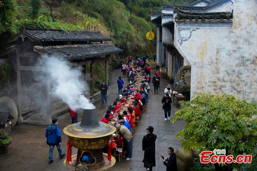 A hot-pot banquet is held on a street in Huangling Ancient Village in Wuyuan County, East China\'s Jiangxi Province, Dec. 22, 2018. The centerpiece of the long-table banquet, a traditional manner in which to celebrate some major festivals and entertain guests, is a giant copper pot measuring three meters in height and two meters in diameter. Visitors, including some from Singapore and Malaysia, joined the feast, where the tables extended for 100 meters. (Photo: China News Service/Fang Huabin)