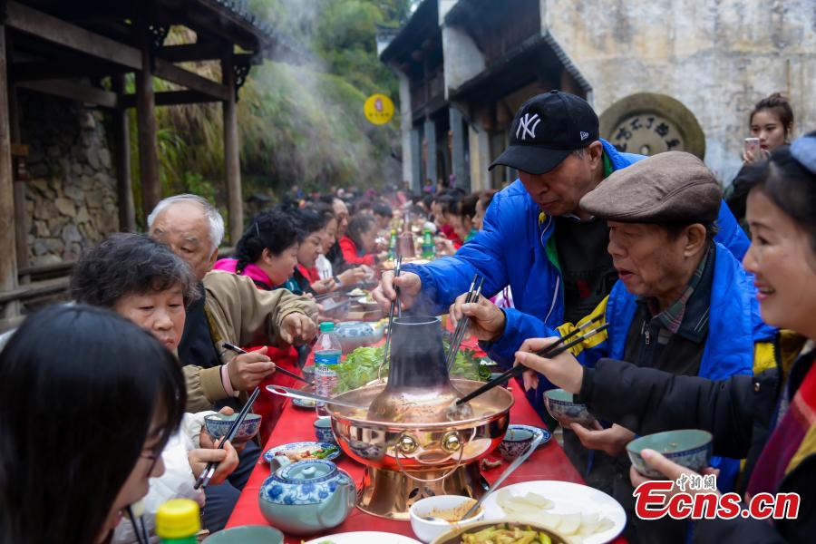 A hot-pot banquet is held on a street in Huangling Ancient Village in Wuyuan County, East China\'s Jiangxi Province, Dec. 22, 2018. The centerpiece of the long-table banquet, a traditional manner in which to celebrate some major festivals and entertain guests, is a giant copper pot measuring three meters in height and two meters in diameter. Visitors, including some from Singapore and Malaysia, joined the feast, where the tables extended for 100 meters. (Photo: China News Service/Fang Huabin)