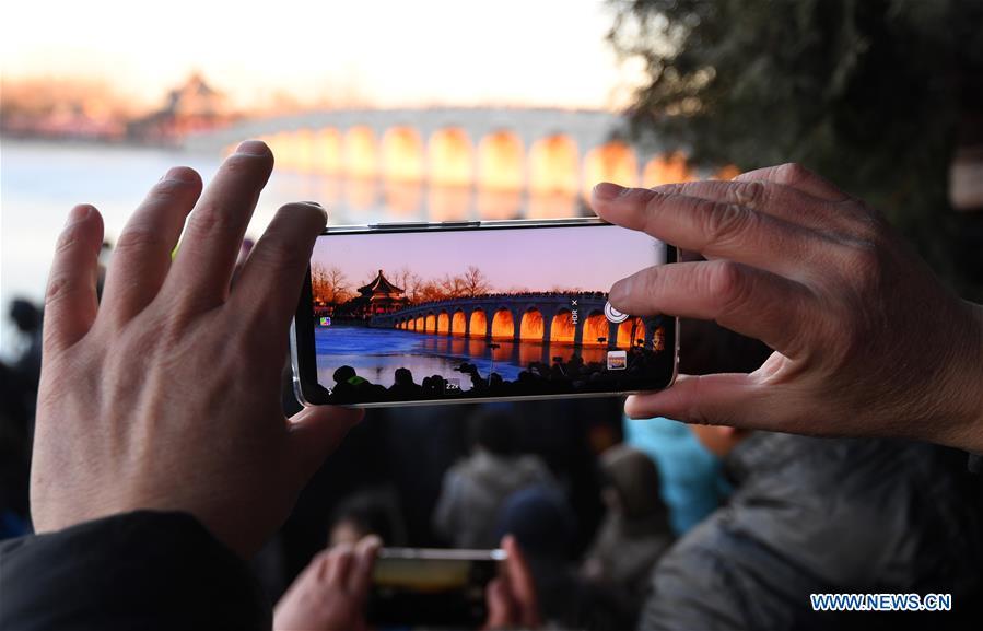 A visitor takes photos of the Qikong Bridge with sunset glow shining through its holes at the Summer Palace in Beijing, capital of China, Dec, 23, 2018. (Xinhua/Chen Yehua)
