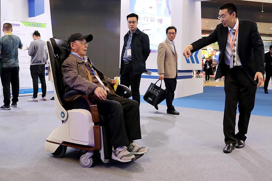 An employee helps a visitor to experience a multi-functional wheelchair designed for elderly healthcare at a fair in Shanghai. (Photo/Xinhua)