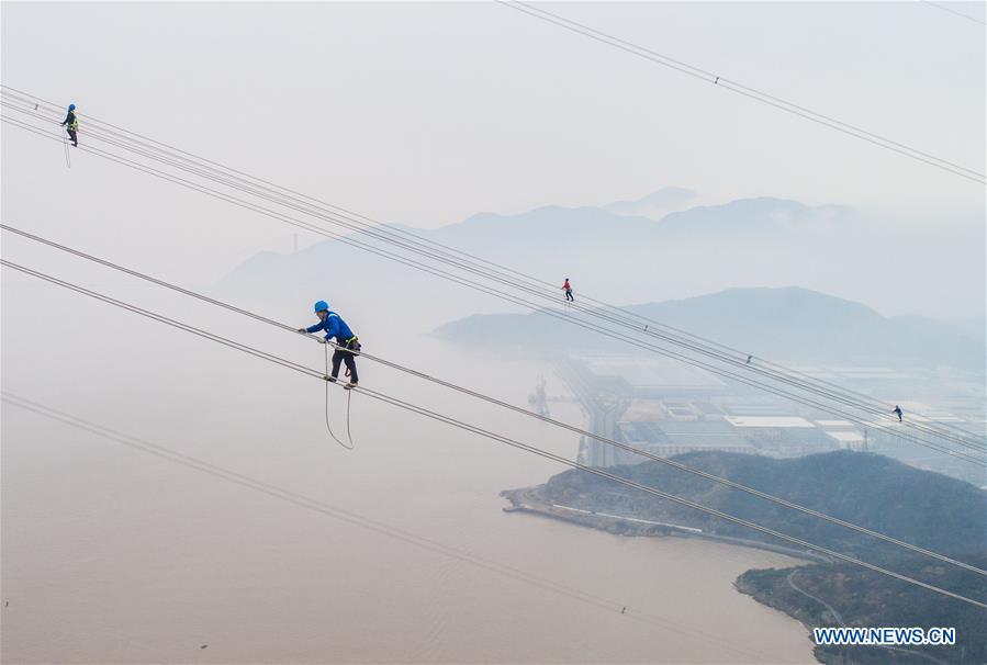 Staff members work on the cables at the site of the giant power supply pylons in Zhoushan, east China\'s Zhejiang Province, Jan. 3, 2019. The two 380-meter-tall pylons carry power cables between Zhoushan\'s Jintang and Cezi islands, a distance of 2,656 meters. The new pylon project is a part of a new ultra-high voltage power line project between cities of Zhoushan and Ningbo. (Xinhua/Xu Yu)