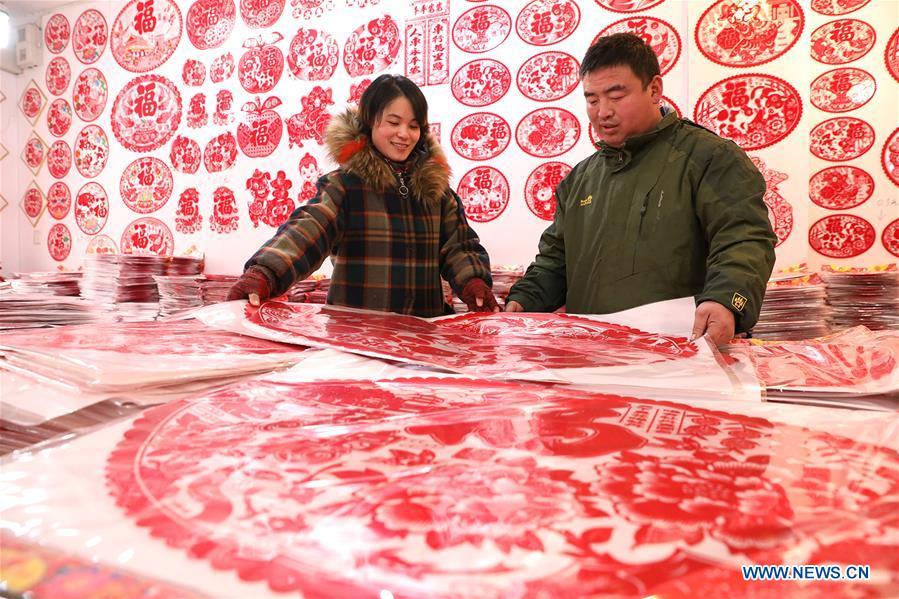 A customer (R) selects New Year goods at a market in Shijiazhuang, north China\'s Hebei Province, Jan. 6, 2019. People are busy buying decorations such as Spring Festival couplets and lanterns to greet the upcoming Lunar New Year. (Xinhua/Liang Zidong)