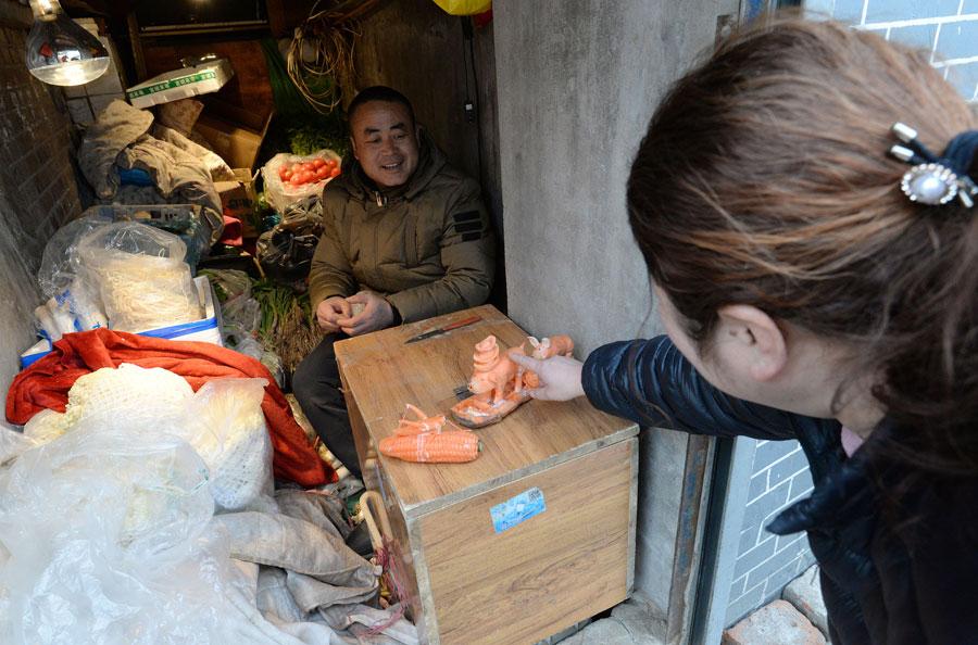A customer shows interest in sculptures carved out of carrots by Guo Yuhong, a Hebei vegetable vendor. (Photo by Hao Qunying for chinadaily.com.cn)
